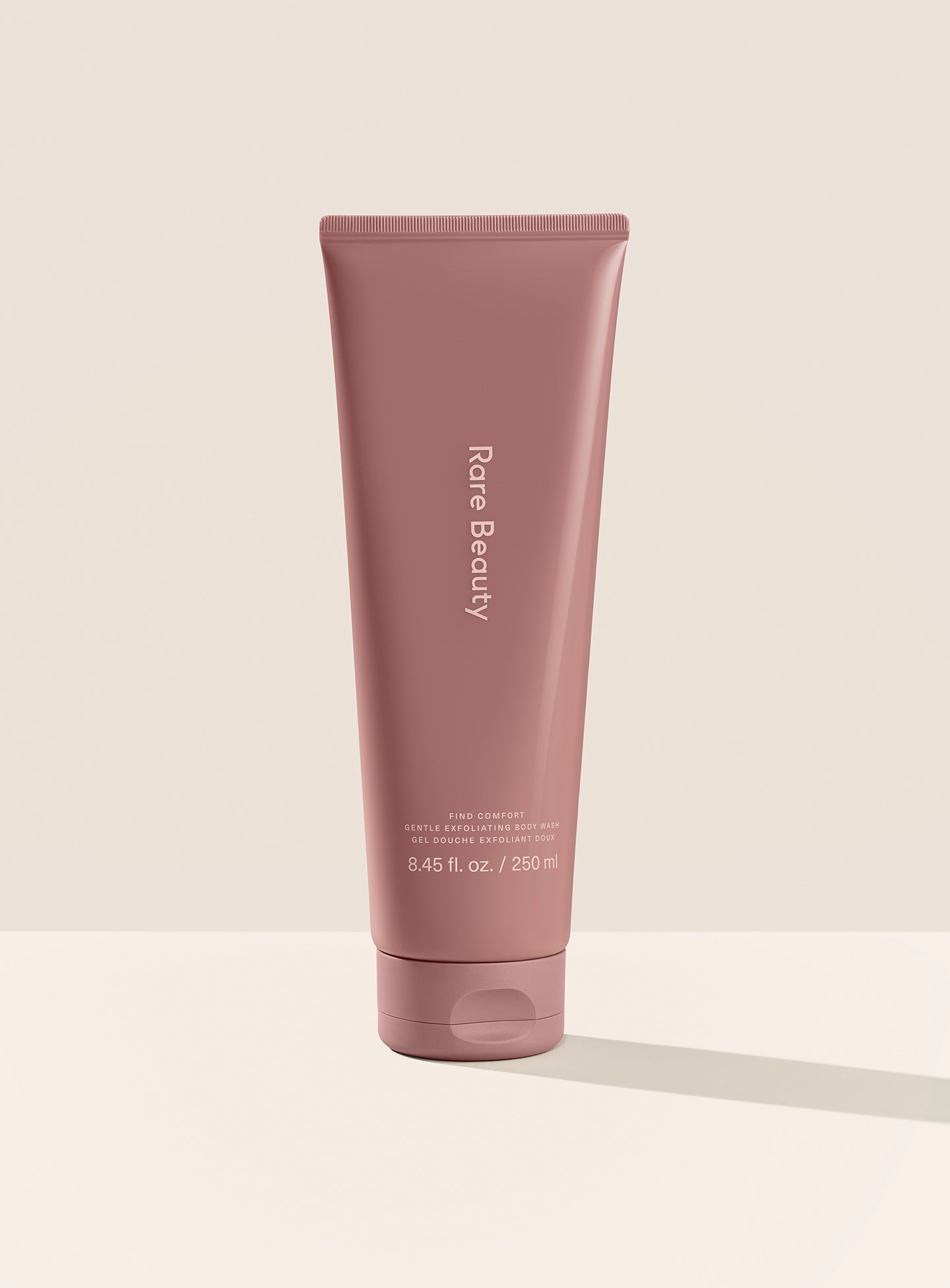 Rare Beauty's Find Comfort Gentle Exfoliating Body Wash standing on a white surface against a white background.